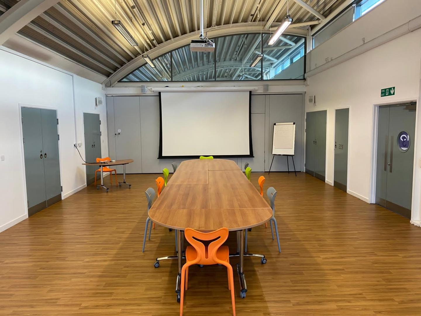 A conference room with wooden floors and a long wooden table with orange chairs